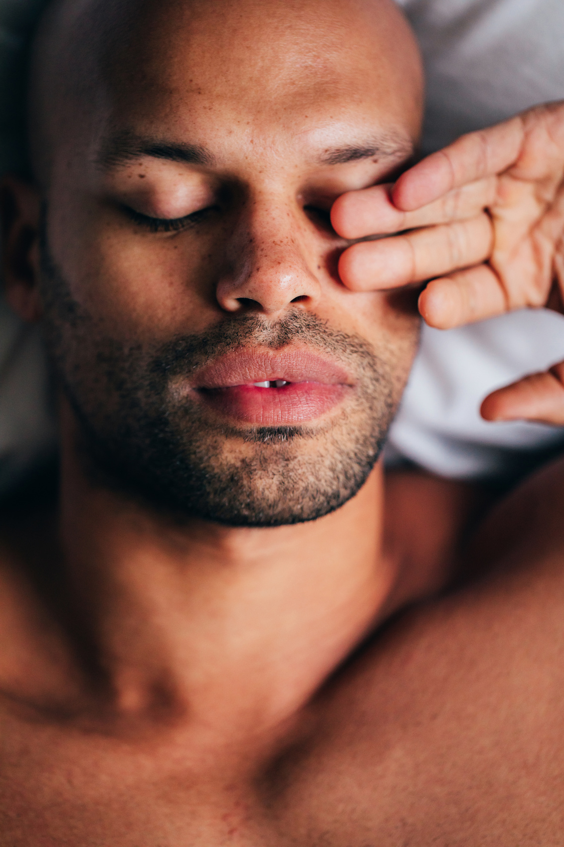 Man resting peacefully in bed at first light, hand near his face