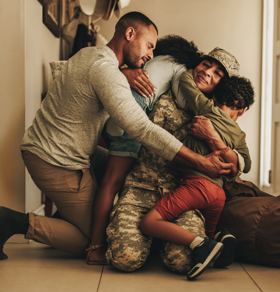 Service member kneeling in a homecoming embrace with her family
