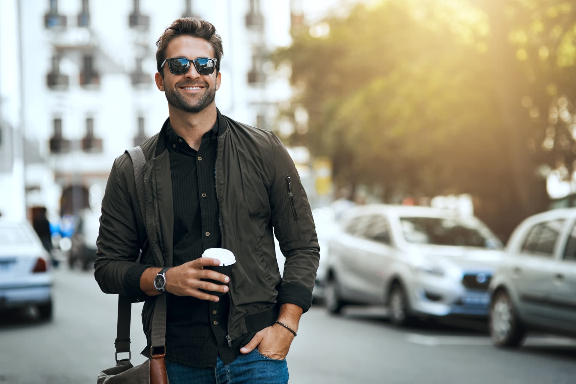 Confident man smiling on a sunlit city street with a coffee