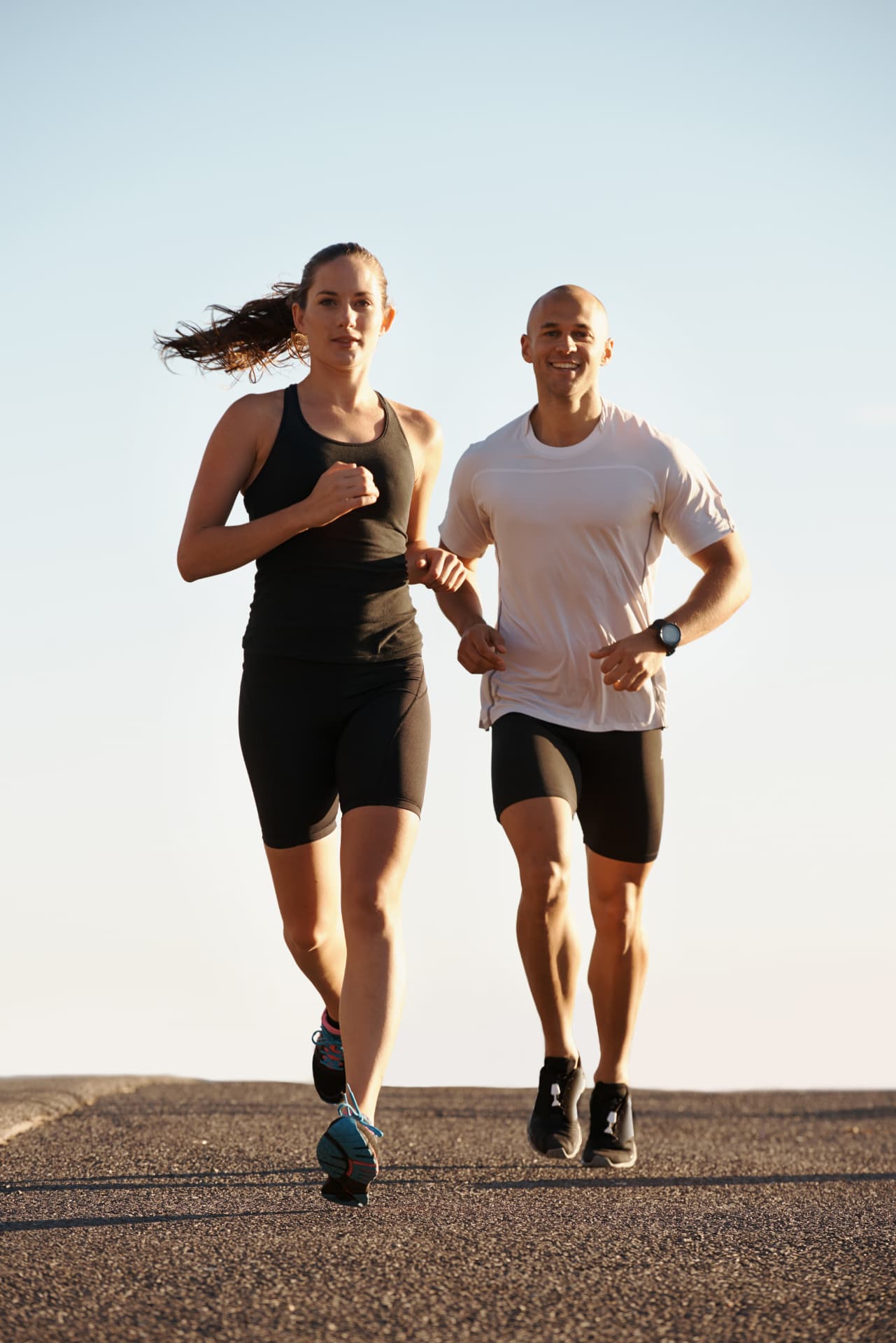 Man and woman running together on an open road at sunrise
